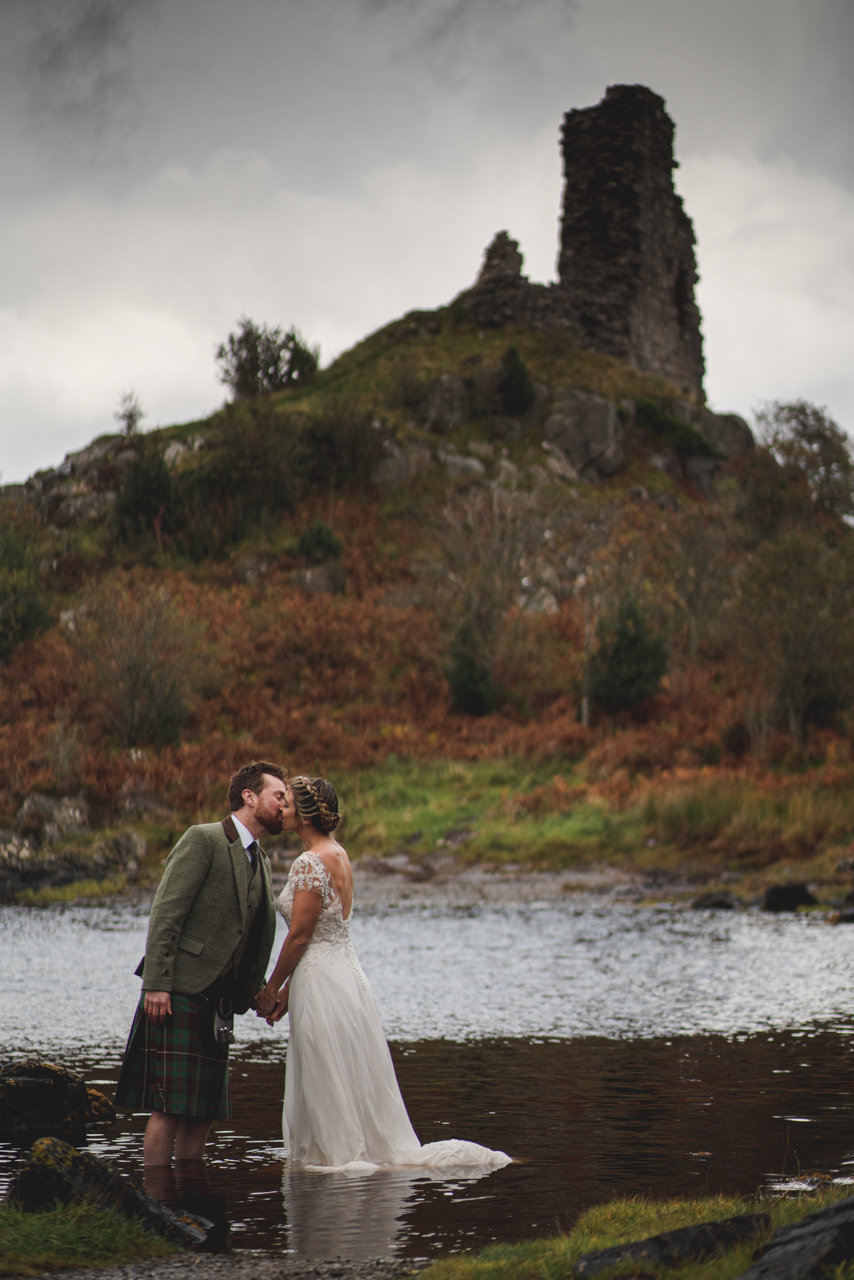 newly married couple posed in a river, in front of a ruined castle on the isle of skye showing What style of wedding photography works on the Isle of Skye?