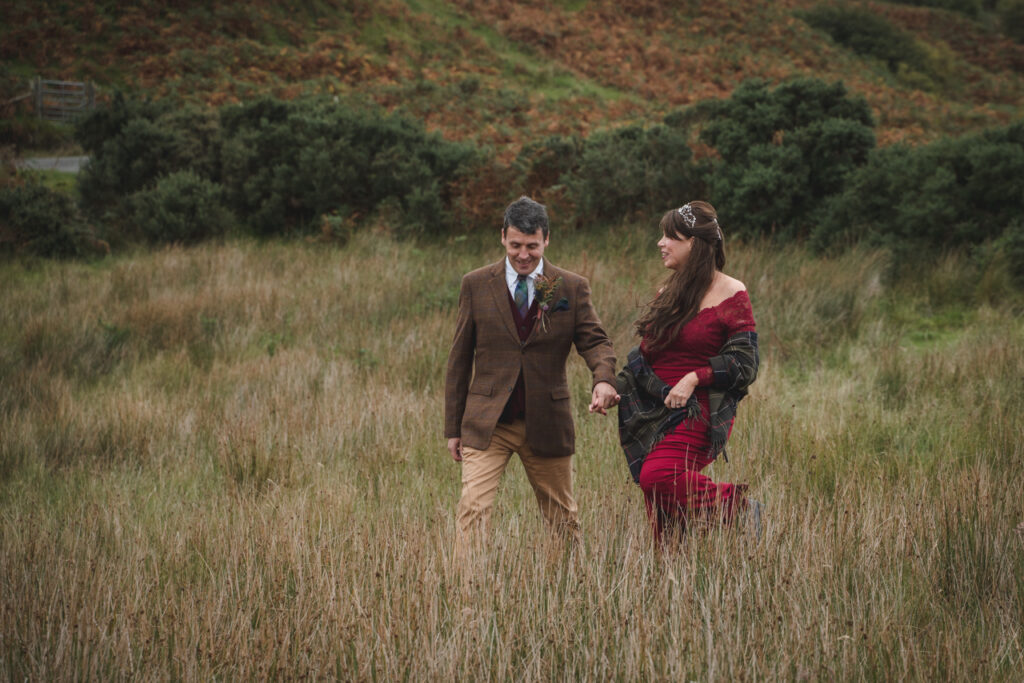 couple walking hand in hand on the Isle of skye, bride wearing a red dress