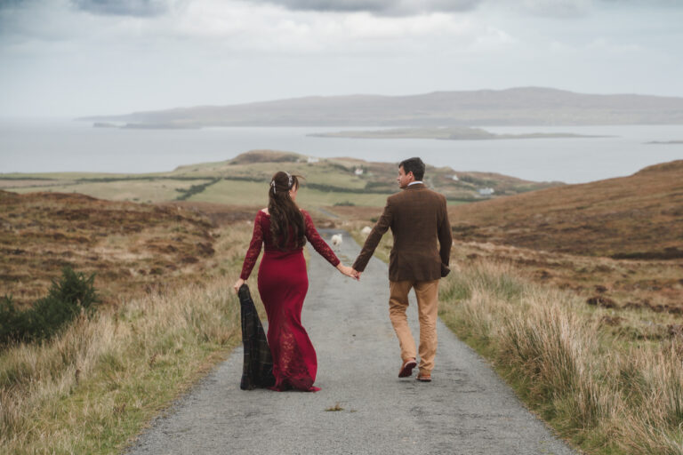 couple walking hand in hand down a country road with bride in a red dress for a wedding on The Isle of Skye