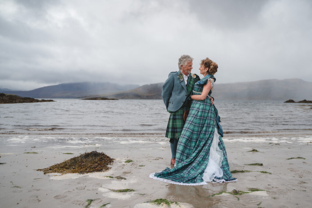Bride and groom on sandy beach on The ISle of Skye. The bride wears a tartan wedding dress.