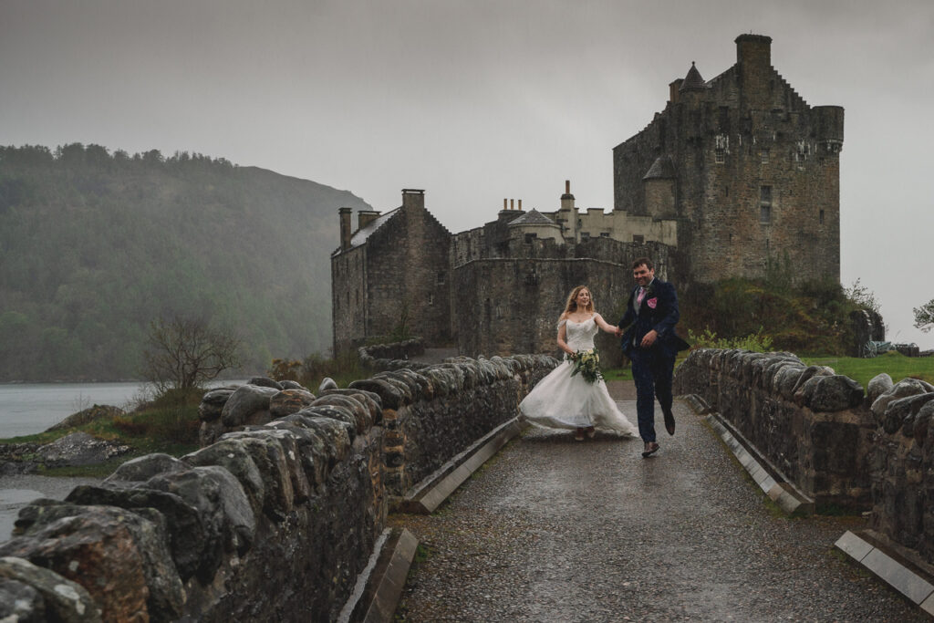 Bride and groom running in the rain across the bridge at Eilean Donan Castle