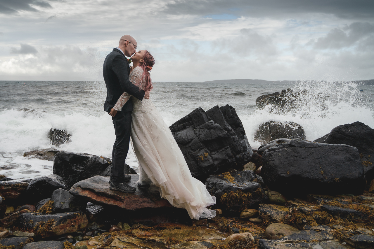 Couple kissing on rocks with waves crashing behind On Isle of Skye elopement