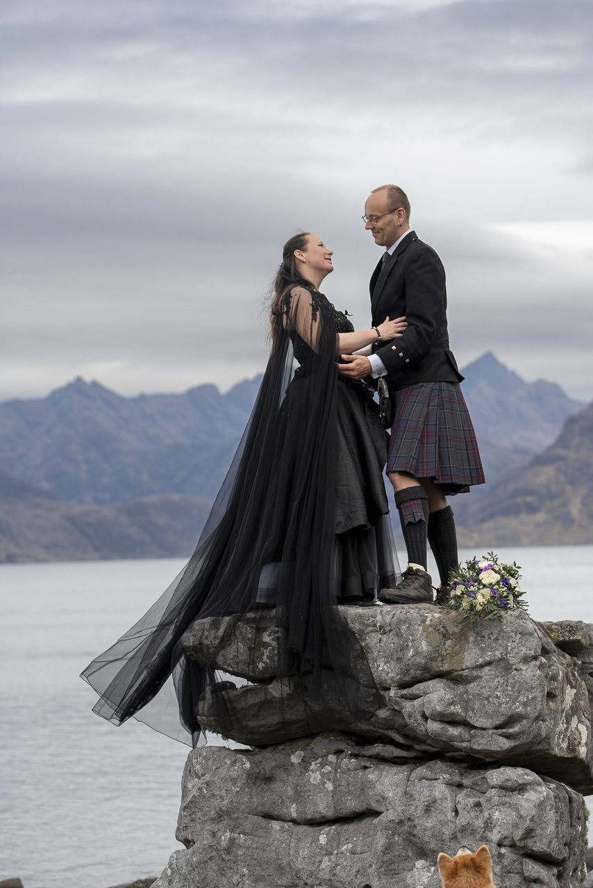 What style of wedding photography works on the Isle of Skye? A couple dressed in black posed on a rock, in a traditional photography style