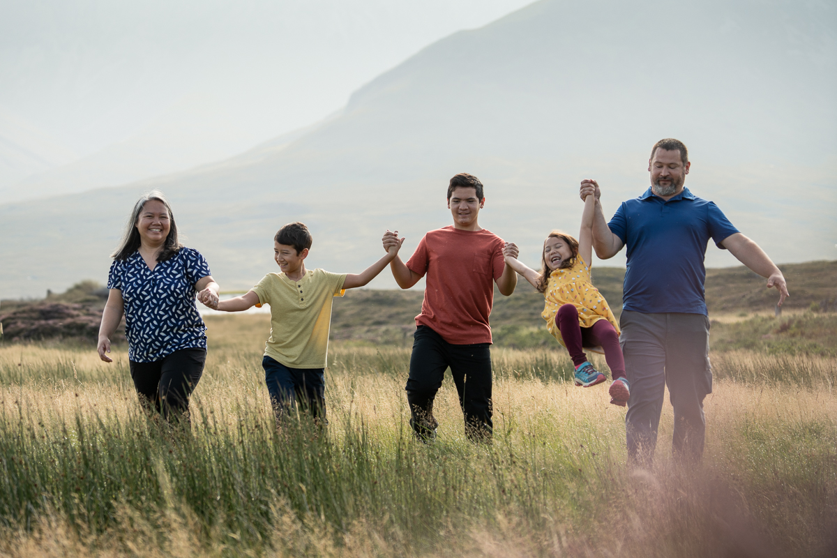What to wear for a family photoshoot on the Isle of Skye family walking across a field with children laughing with joy on the Isle of Skye